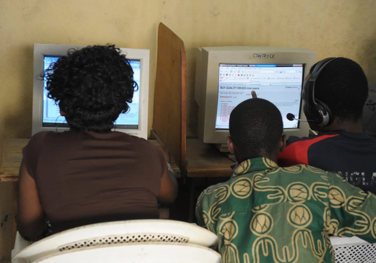 Trois personnes de dos devant les écrans d'un cybercafé, l'un affichant une publicité pour des médicaments